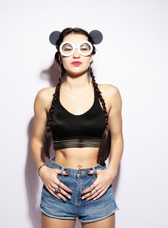 Cheerful young brunette woman with braids and big sunglasses looks and smiles over white background.の写真素材
