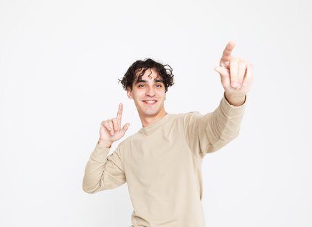 A cheerful smiling young man in a beige sweater dances on a white studio background, enjoys lifeの写真素材