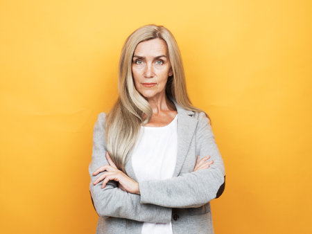 lifestyle, emotion and old people concept: Portrait of beautiful senior woman with long hair with crossed arms over yellow background.の写真素材