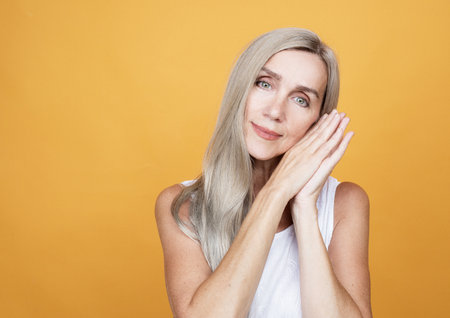 Beauty portrait of mature woman smiling with hand on face over yellow backgroundの写真素材
