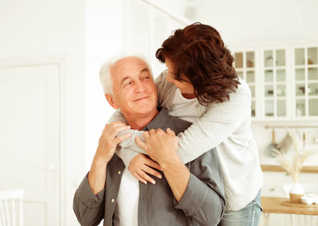 Portrait of cute happy Caucasian couple of retired husband and wife hugging indoors. Relationship, people and family concept.の写真素材