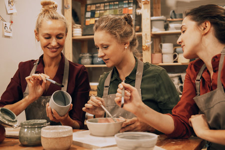 A company of three cheerful young women friends are painting ceramics in a pottery workshop.の写真素材