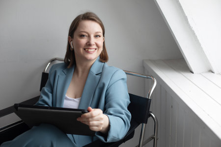 Young smiling woman sitting at the window at home with digital tabletの写真素材