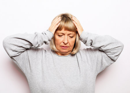 Frustrated nervous middle aged woman touching forehead over white backgroundの写真素材