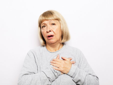 Lifestyle, health and old people concept: An elderly woman holds her hands near her heart, her heart hurts. Pjrtrait over white background.の写真素材