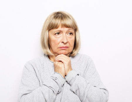 Lifestyle, health and old people concept: An elderly woman holds her hands near her heart, her heart hurts. Pjrtrait over white background.の写真素材