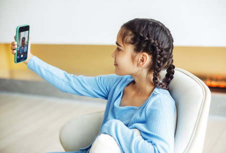 Little kid girl sitting on chair, using smartphone, take selfie. Kids and gadgets concept.の写真素材