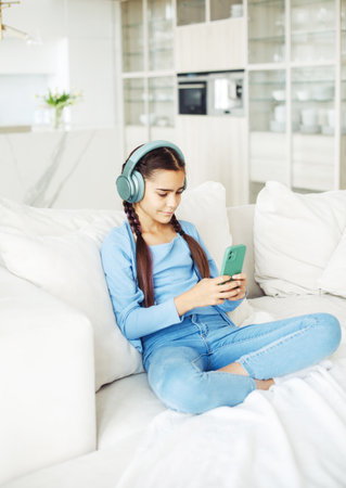Little kid cute girl sitting on sofa, using smartphone with headphones, take selfie. Kids and gadgets concept.の写真素材