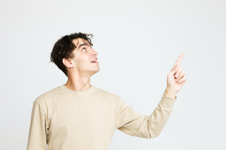 Young brunette man shows something with finger up over white background.の写真素材