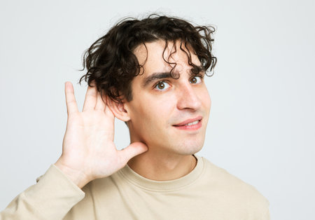 Young handsome brunette man hearing something and smiling over light gray background.の写真素材