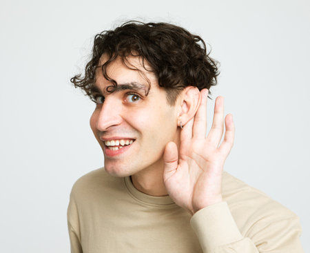 Young handsome brunette man hearing something and smiling over light gray background.の写真素材