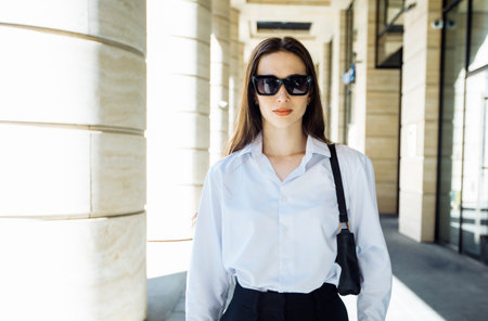 Portrait of a stylish young woman with long hair in a white blouse and sunglasses.Modern fashion. Street fashion.の写真素材