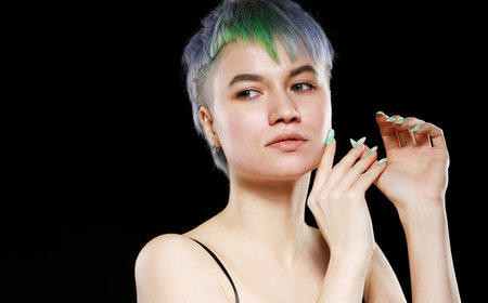 Beautiful young woman with stylish short haircut and colored hair dyeing - blue-green hair. Close-up portrait over black background.の写真素材