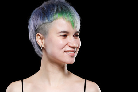 Beautiful young woman with stylish short haircut and colored hair dyeing - blue-green hair. Close-up portrait over black background.の写真素材