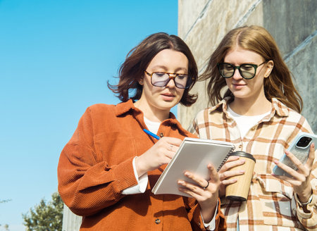 Two female student friends with a notebook and a coffee to go discuss their studiesの写真素材