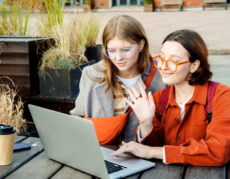 Two young female student friends with laptop at table near college campusの写真素材