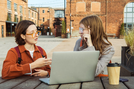 Two young female student friends with laptop at table near college campusの写真素材