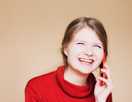 Portrait young happy smiling surprised woman talking on mobile phone, listening to good news, communicating with friends or calling clients isolated on beige studio background.の写真素材