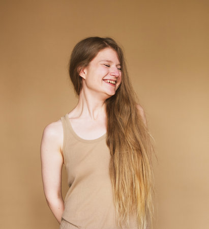 cheerful happy young woman laughing sincerely on beige background.の写真素材