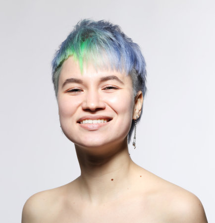 Beautiful young woman with stylish short haircut and colored hair dyeing - blue-green hair. Close-up portrait over light gray background.の写真素材