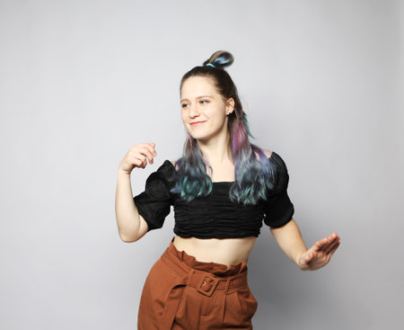 Cheerful young woman with curly colored hair dancing on light gray background, enjoying the dance.の写真素材