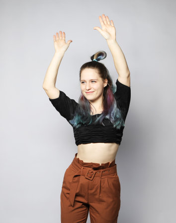 Cheerful young woman with curly colored hair dancing on light gray background, enjoying the dance.の写真素材