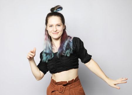 Cheerful young woman with curly colored hair dancing on light gray background, enjoying the dance.の写真素材