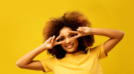 Young african american woman covering eye with victory v-sign gesture isolated on yellow color background.の写真素材