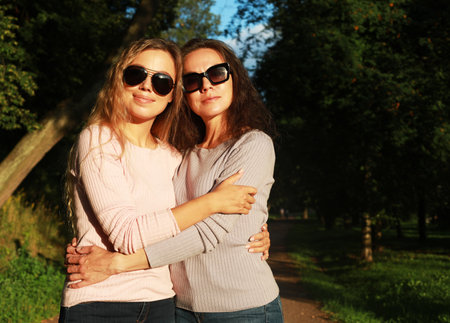 Mother With Adult Daughter wear sunglasses In Park Together. Love and happy. Sunset time, golden hour.の写真素材