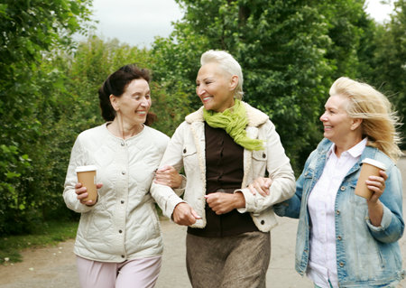 Friendship is priceless. Three elderly ladies in casual clothes are walking in the park. Coffee and socializing, friendship in retirement.の写真素材