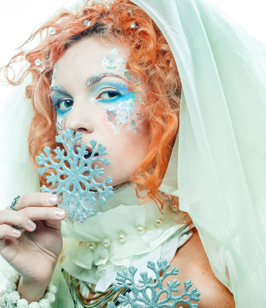 woman with a bright creative make-up in a New Years style holds a silver snowflake near her face.の写真素材