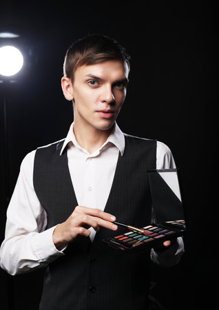 Professional makeup artist male posing in studio, holds a palette and brushes. Dark background.の写真素材