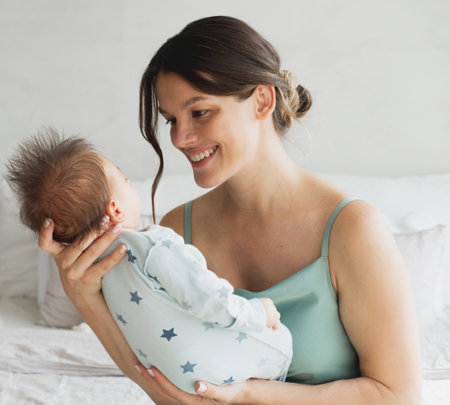Portrait of a newborn baby with young happy mother on the bed.