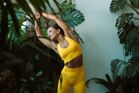 Woman practices yoga at home among flowers. Urban jungle and gymnastics, yoga, pilates.の写真素材