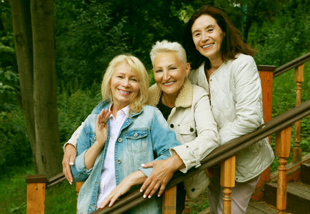 Three pensioners, cheerful women friends, posing on the stairs in a summer parkの写真素材