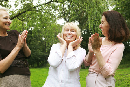 Women friends in the park celebrate a birthday. Clap your hands, congratulate, rejoice. Happy summer day.の写真素材