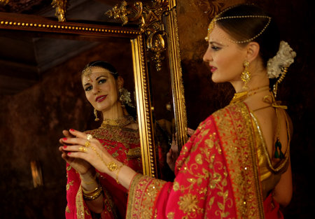 Female model Hindu Bride in saree, wearing gold and jasmine flower garlands in the hair near mirrorの写真素材