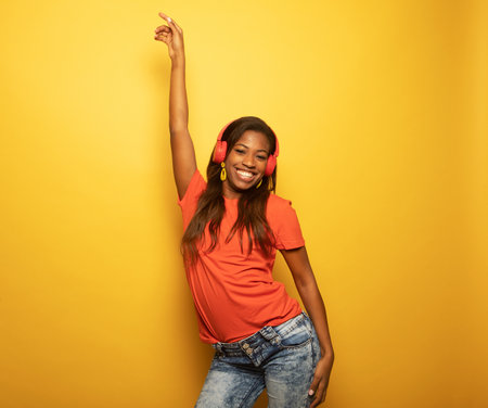 Stunning african woman with light-brown skin relaxing in headphones over yellow background.の写真素材