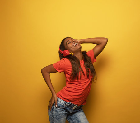 Enthusiastic mix race woman with long hair listening favorite music by headphones over yellow background.の写真素材