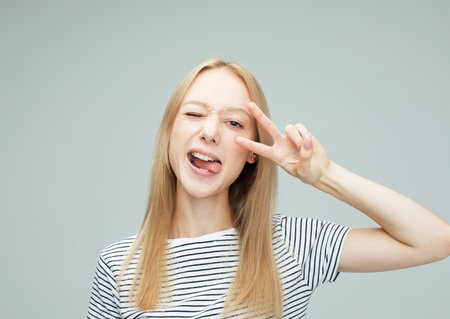Young woman laugh and showing peace or victory sign at camera. Emotion and feelingsの写真素材