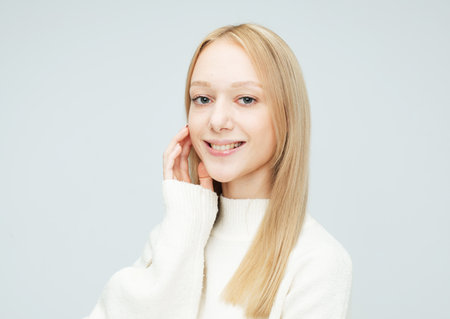Attractive young woman with blond hair smiling isolated over light gray color background.の写真素材