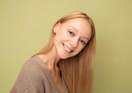 cheerful woman with blond hair smiling isolated over light olive color backgroundの写真素材