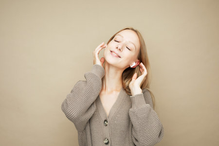 Beautiful young woman in headphones listening to music over beige background.の写真素材