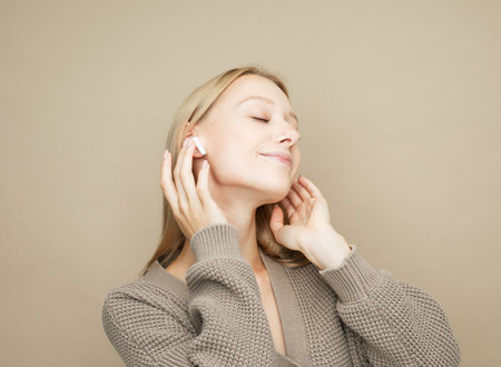 Beautiful young woman in headphones listening to music over beige background.の写真素材