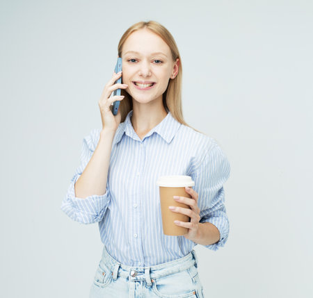 A pretty blonde female model with long hair holds coffee with her and chats on the phone.の写真素材