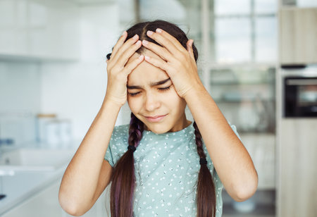 Ten year old girl with headache, tired of homework. Girl at home in modern kitchen. Education and...