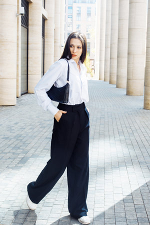 Stylish female model in black pants and white cotton blouse posing outdoor. Female fashion. City lifestyle.の写真素材