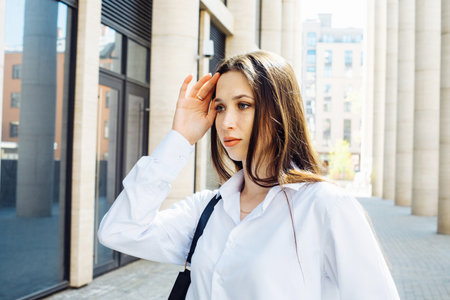 Fashionable brunette woman in the city. Young female model with long hair wears white shirt.の写真素材
