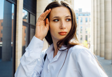 Fashionable brunette woman in the city. Young female model with long hair wears white shirt.の写真素材