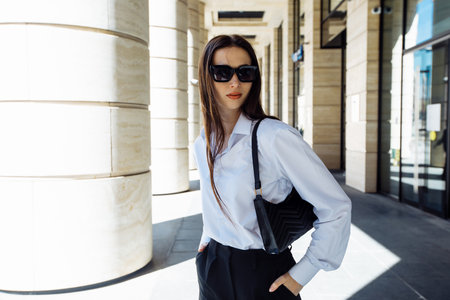 Portrait of a stylish young brunette woman in a white blouse and sunglasses. Modern fashion. Street fashion.の写真素材